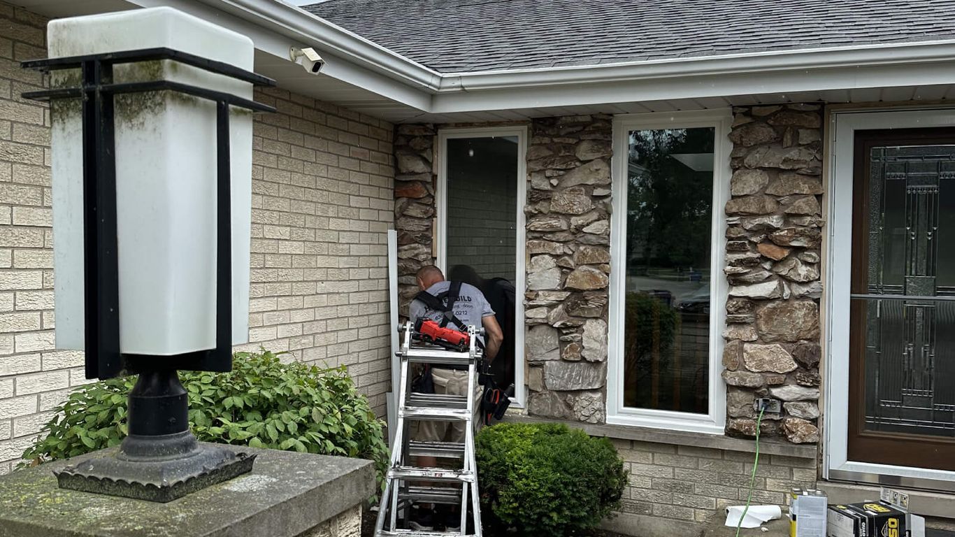 A person works on a house exterior with a ladder and tools.