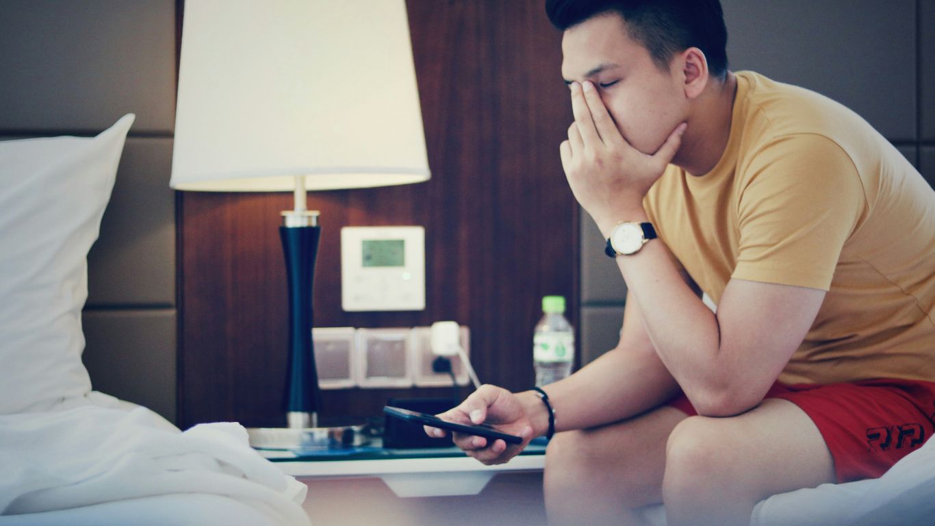 man holding phone and sitting while putting left hand on his face