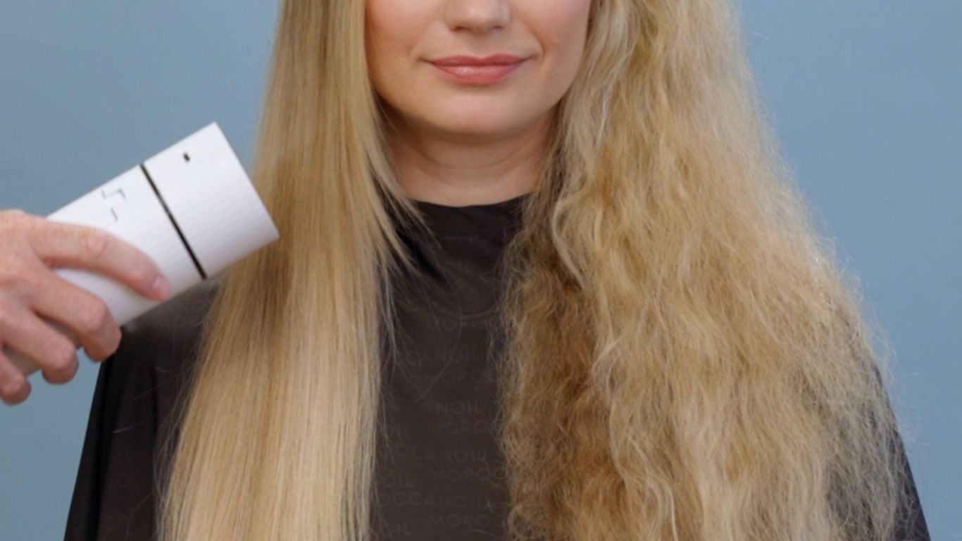 Person with half straight, half curly hair, holding a product.