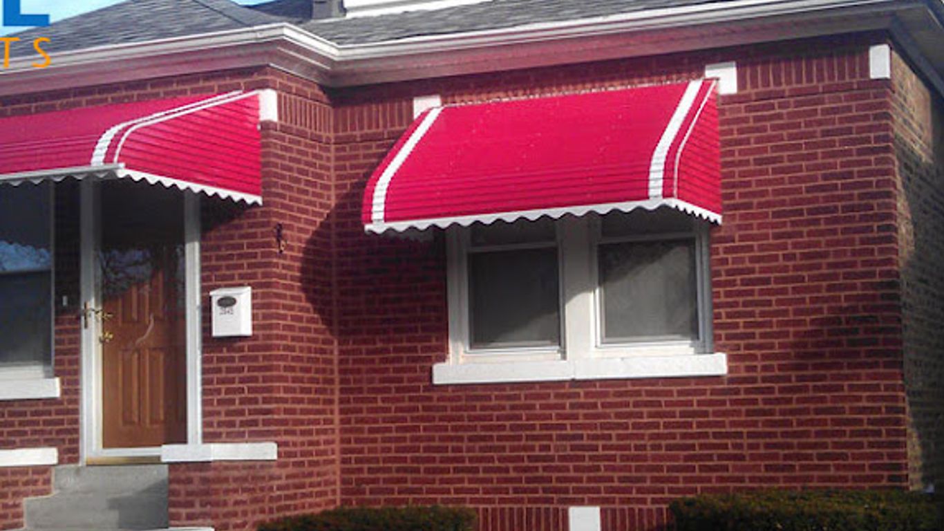 Red awnings over the windows and door of a brick house.