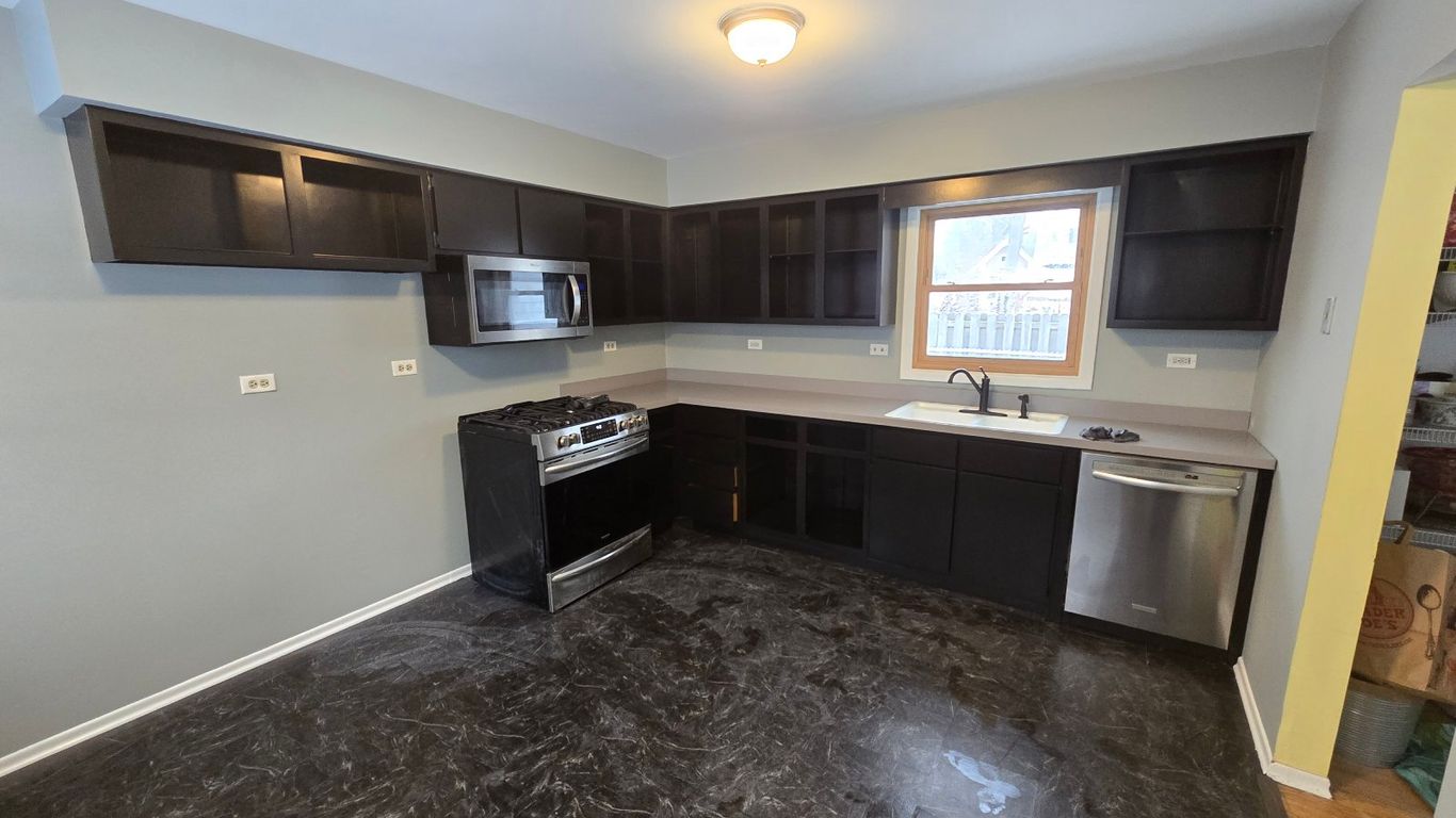 A dark-themed kitchen with dark cabinets, a stainless steel stove, and a patterned floor.