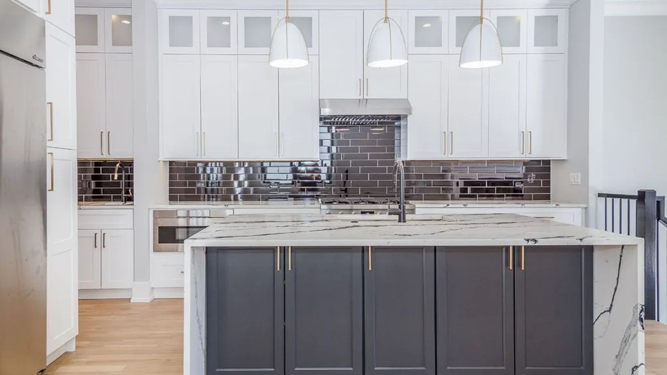 Modern kitchen with white cabinets, dark island, and marble countertop.