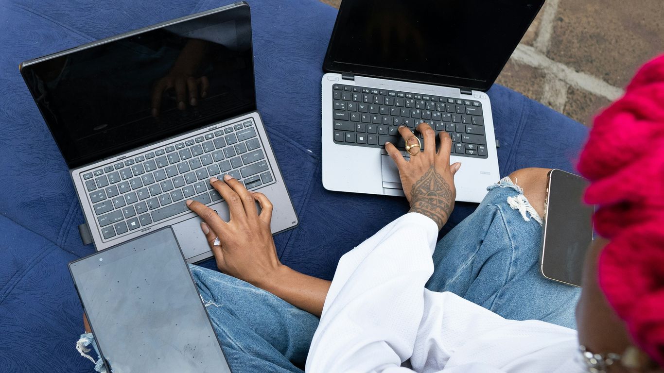 Two people using laptops outdoors on a blue cushion.
