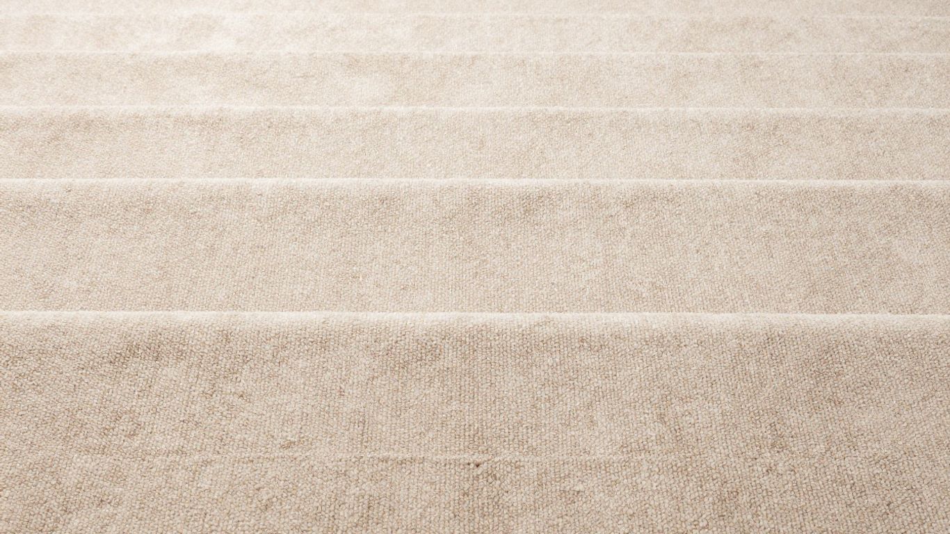 Close-up of beige cut pile carpet texture on stairs.