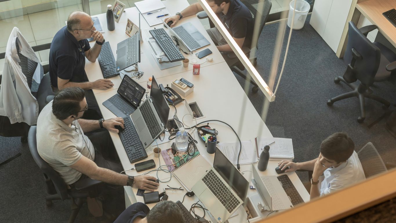 Cuatro personas trabajando en escritorios en una oficina moderna.