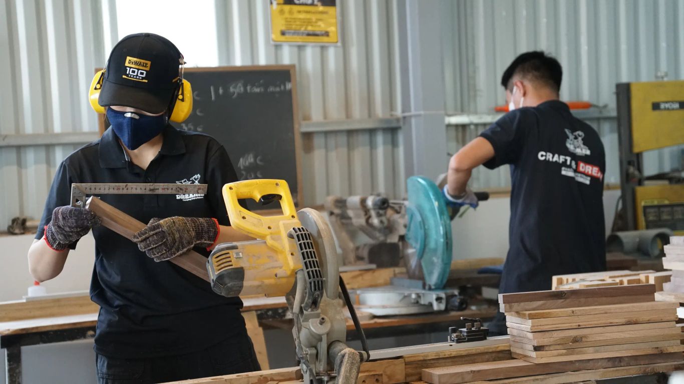 Workers in a workshop using saws and measuring wood.