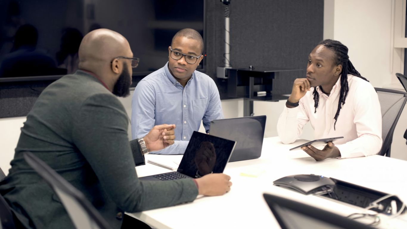 a group of people sitting around a table with laptops