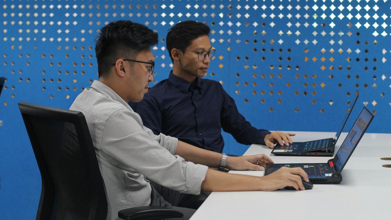 two men sitting at a table with laptops