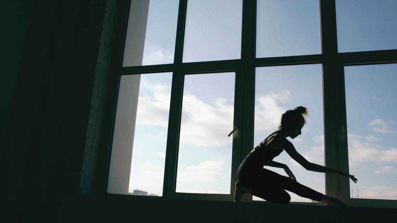 Silhouette of a ballerina stretching by a window.