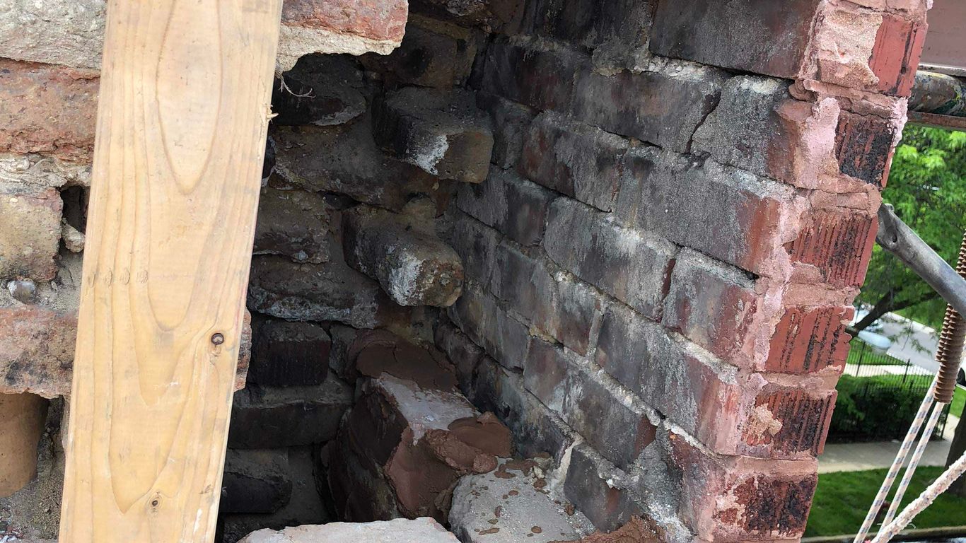 A damaged brick chimney with a hole, undergoing repair with new bricks.