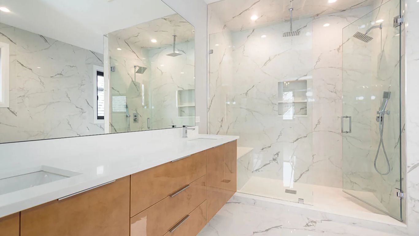 Modern bathroom with marble tiles, glass shower, and wooden vanity.
