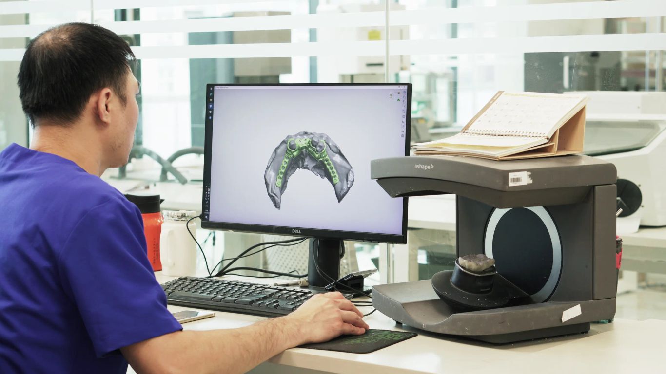 Person using a 3D scanner and computer for dental prosthetics.