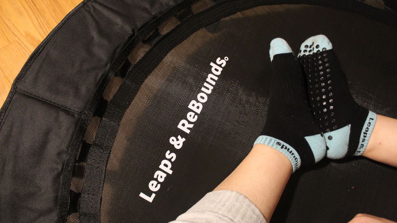 Person wearing grip socks sitting on a mini trampoline, indoors.