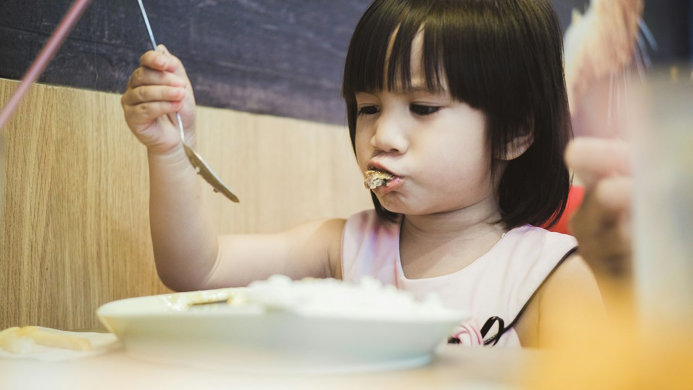 girl eating while holding spoon over plate