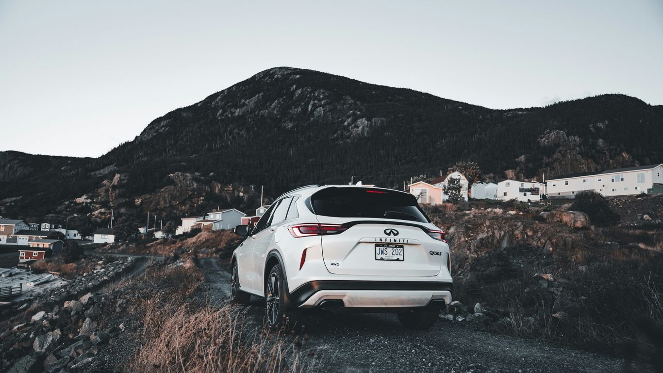 White suv parked on a gravel road near mountains.