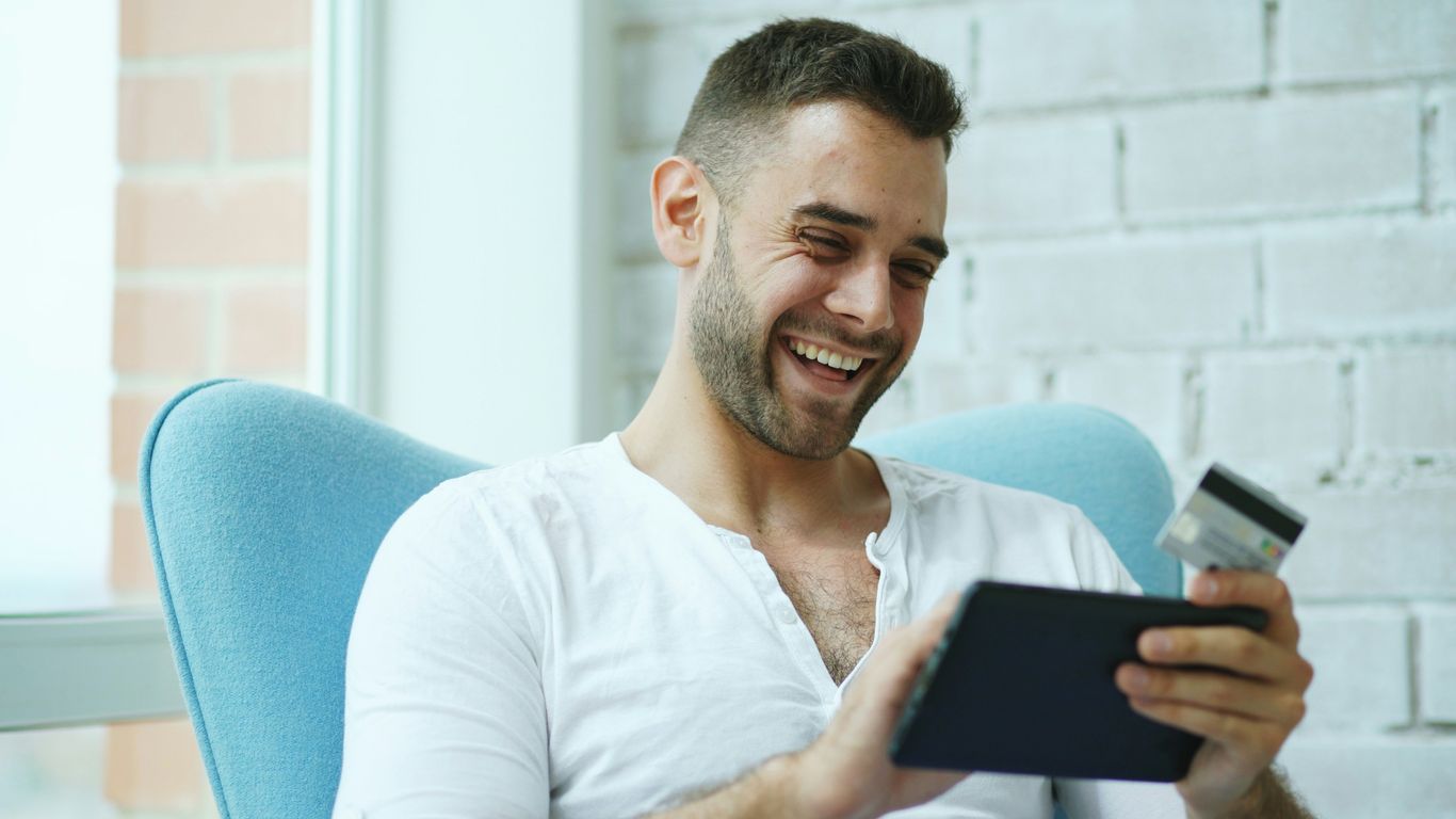 Man laughing while holding credit card and tablet.