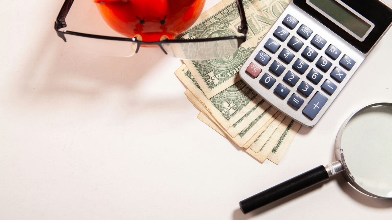 Calculator, magnifying glass, glasses, and money on white surface.