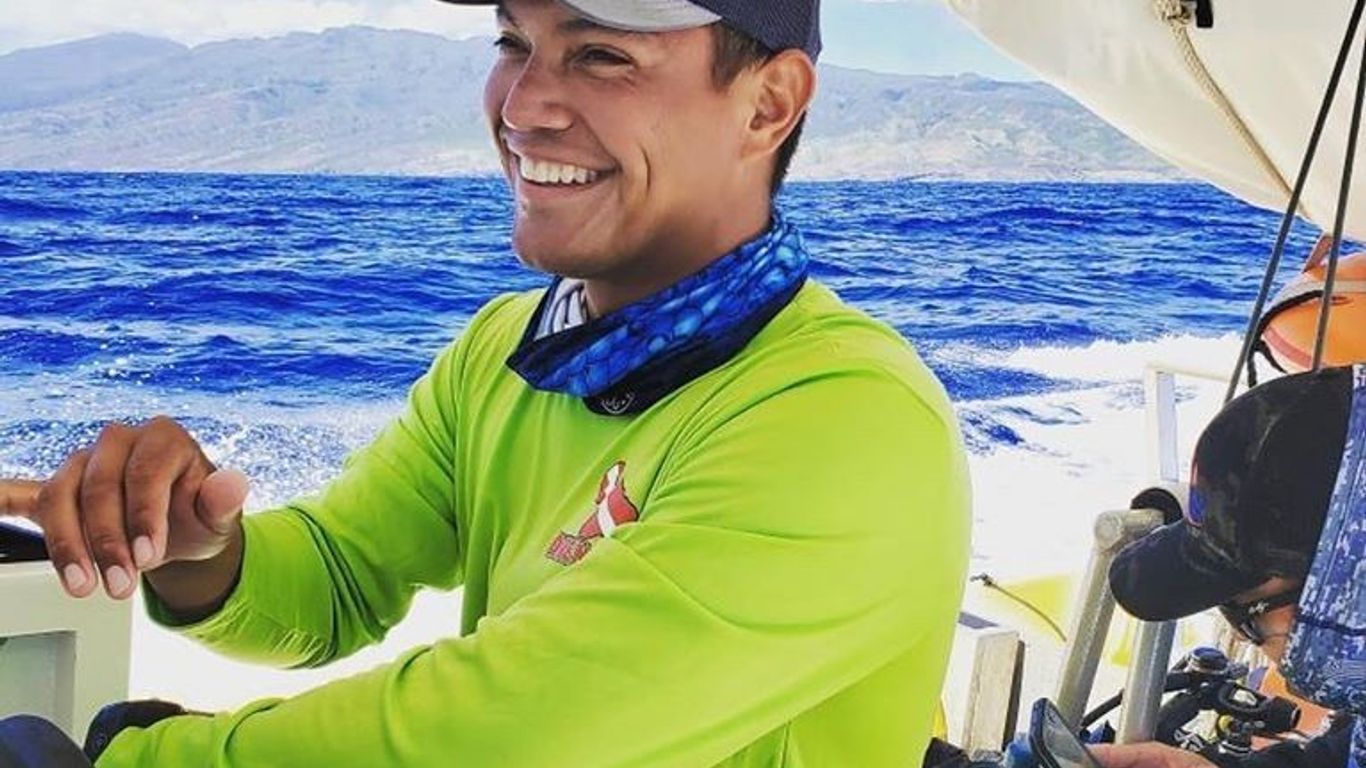 Person steering a boat on a sunny day with islands in the background.