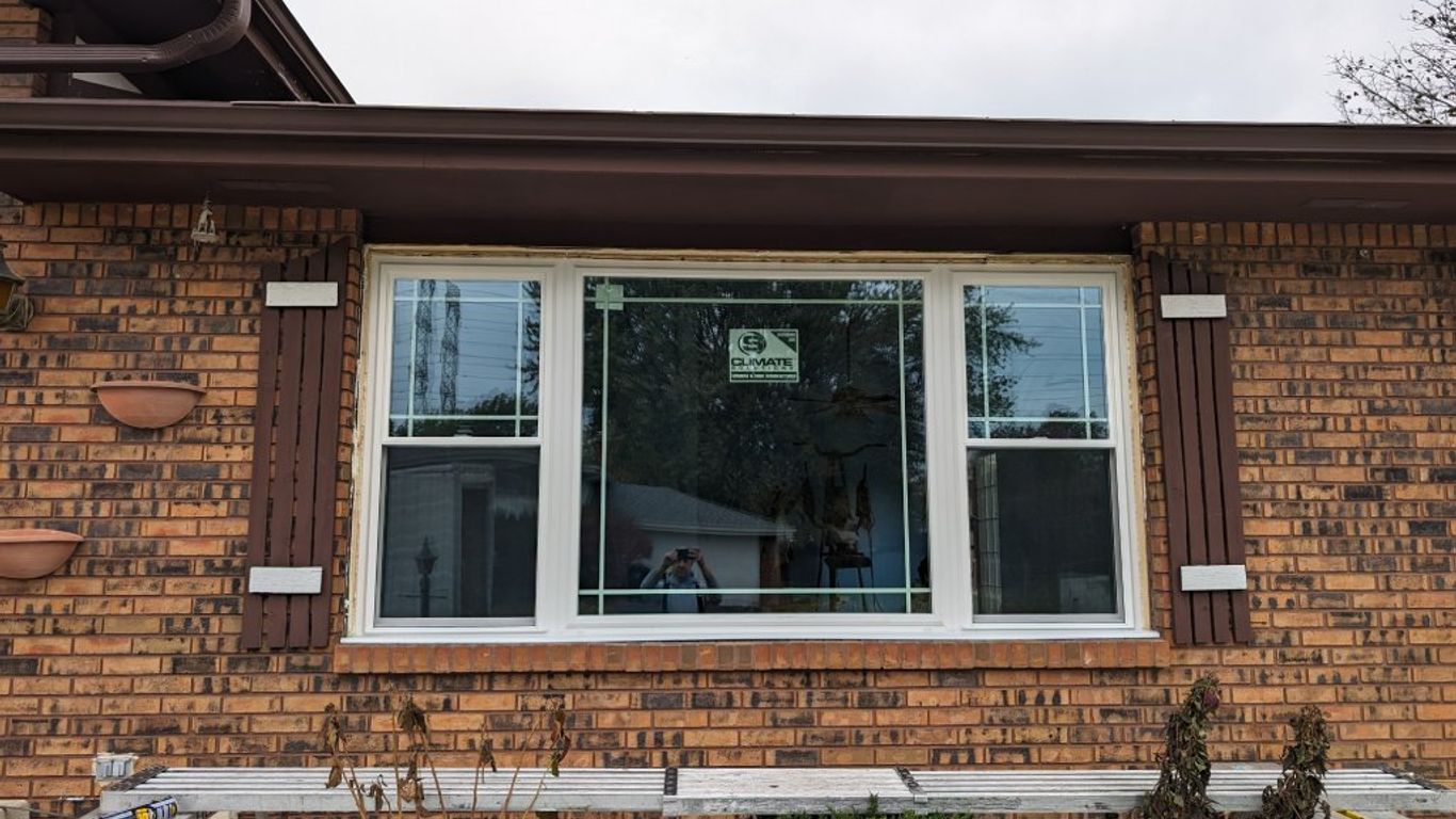 A new window is installed on a brick house with shutters.