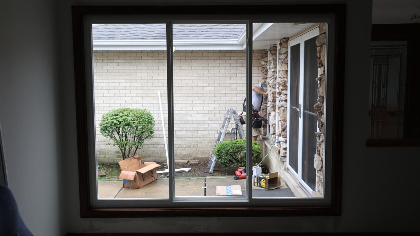 Person working on house exterior through a large sliding glass window.