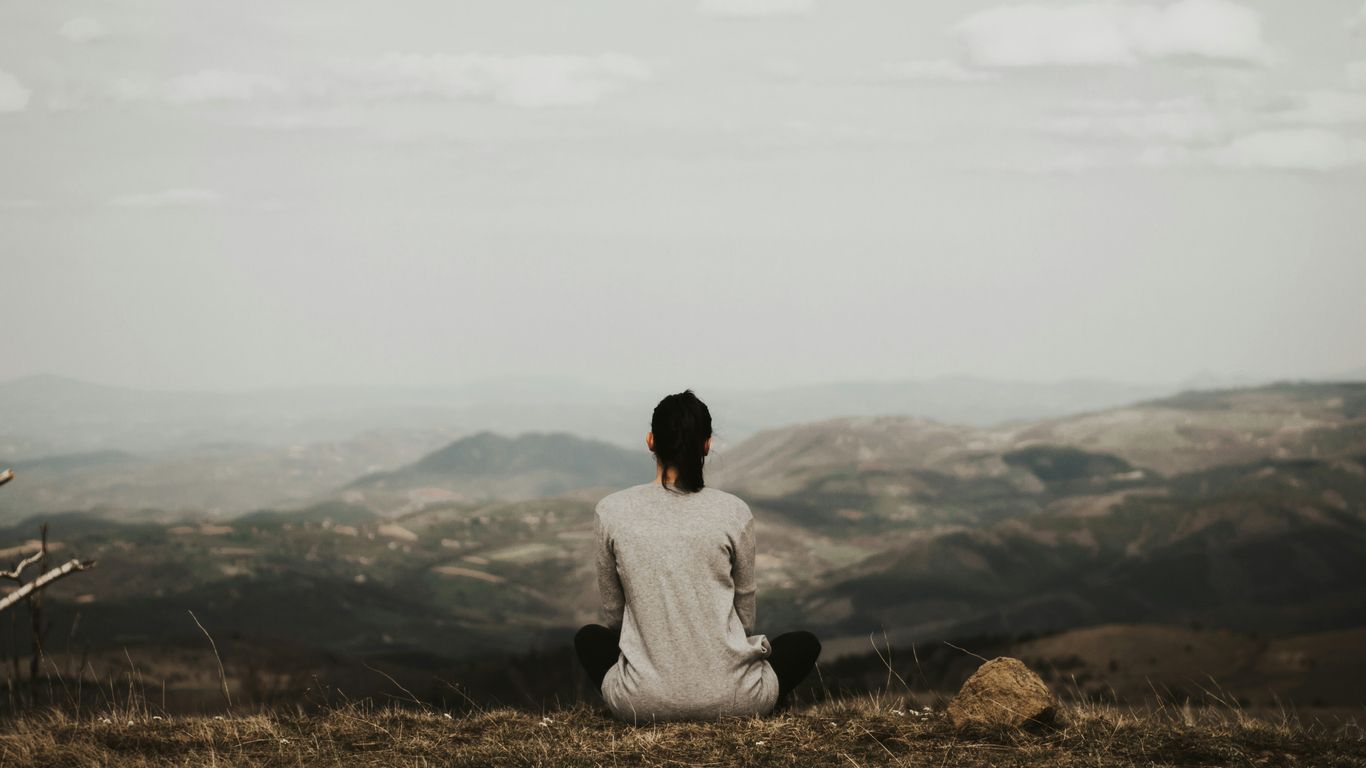 woman sitting on cliff overlooking mountains during daytime
