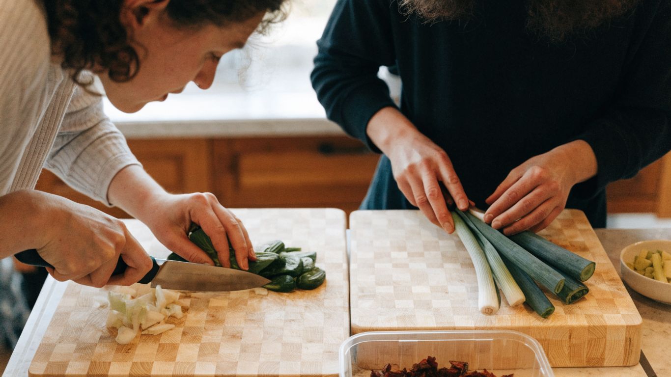 Two cooks prepping vegetables at separate maple boards
