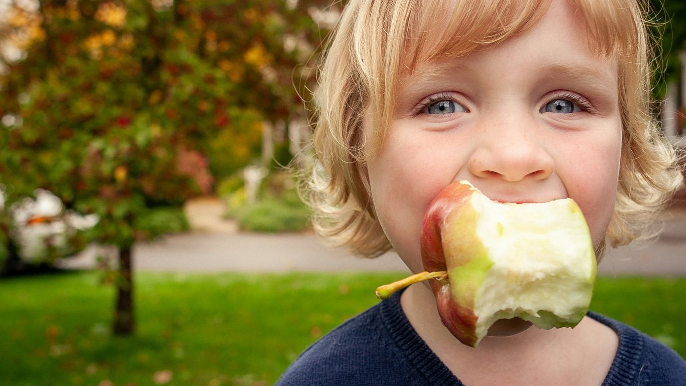 Young child with a bitten apple in mouth