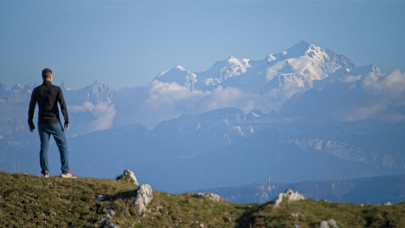 Man standing on a grassy hill overlooking mountains.