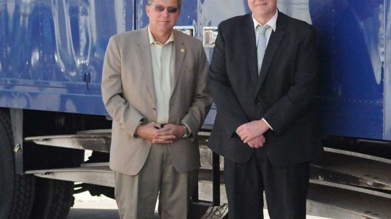 Two men stand in front of a moving truck with 