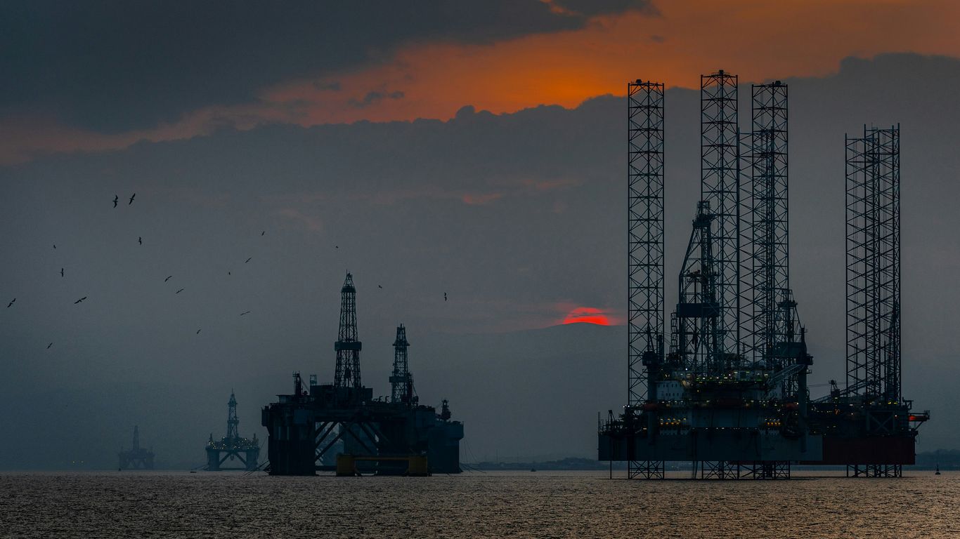 An orange drone over a tall offshore oil rig