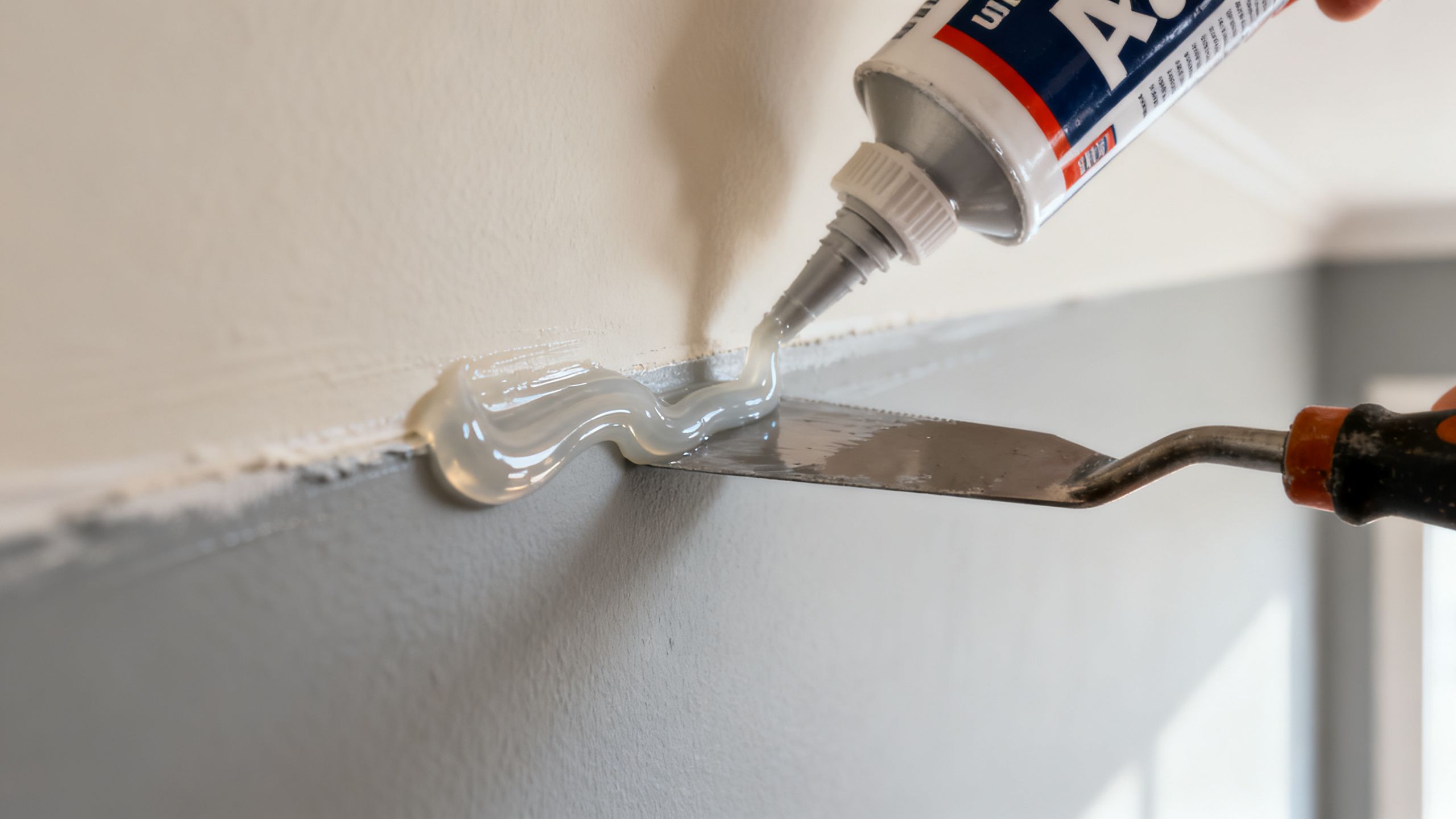 Flexible decorator's caulk being applied and carefully tooled into a wall-ceiling junction