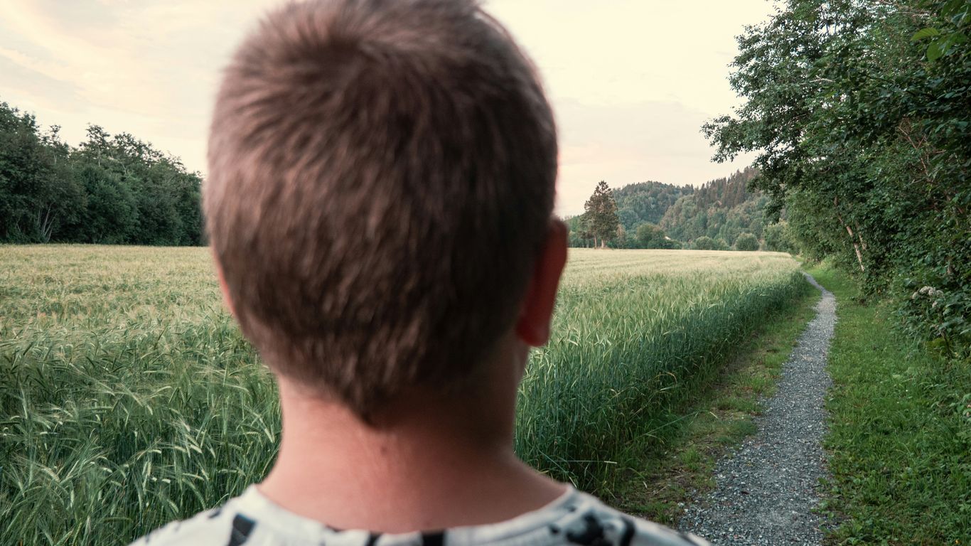 a man standing on a dirt road next to a lush green field