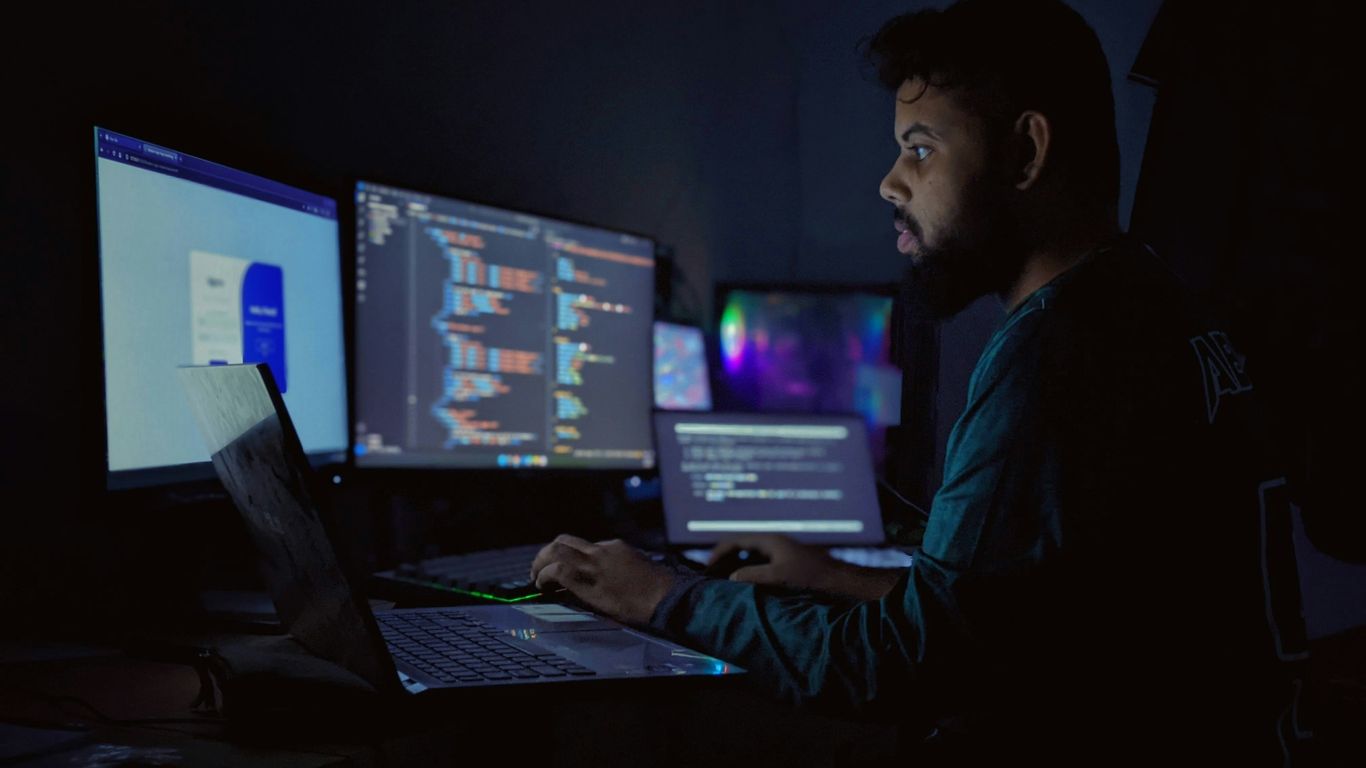 A man sitting in front of three computer monitors