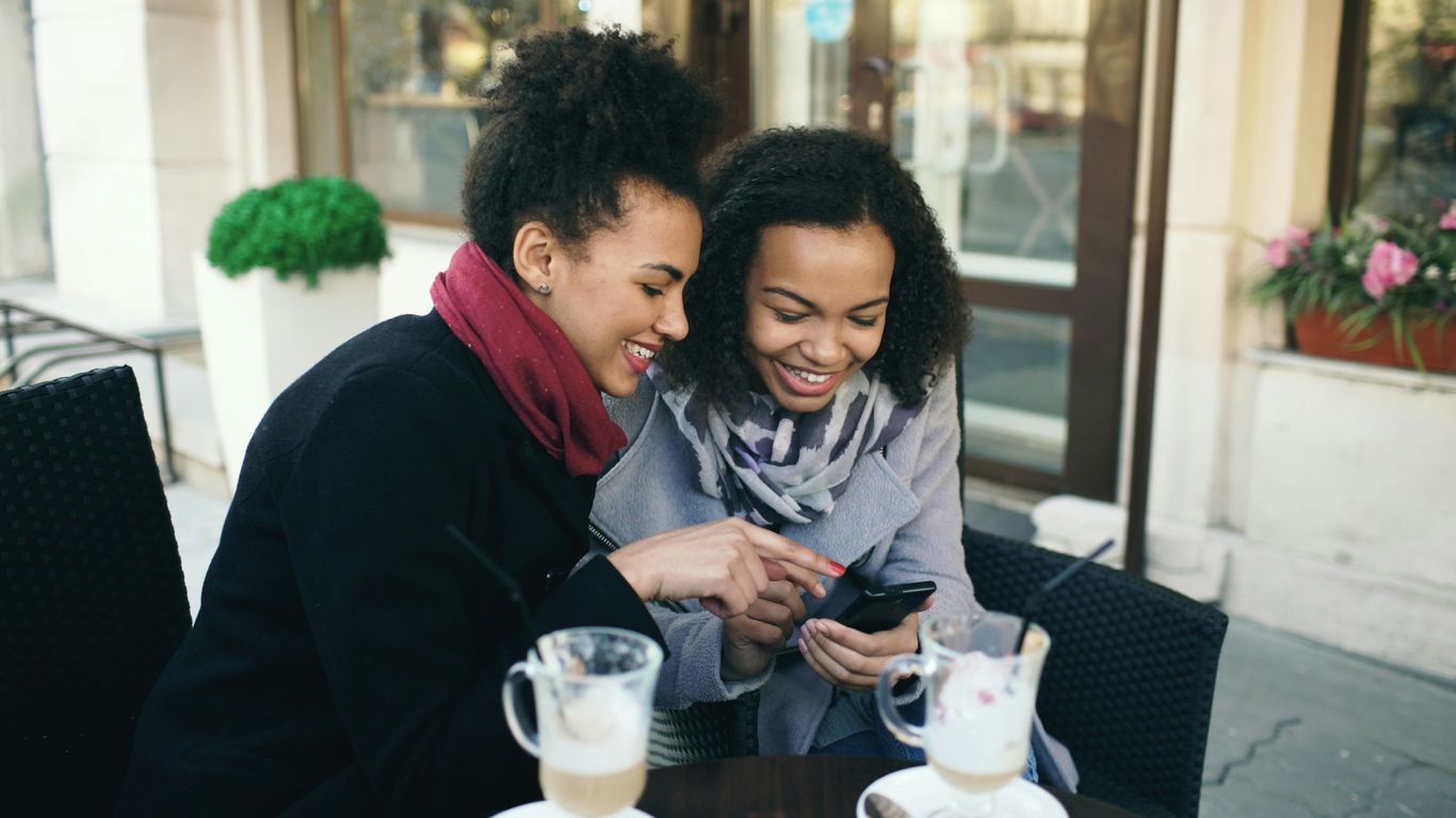 Two women looking at a smartphone together at cafe.