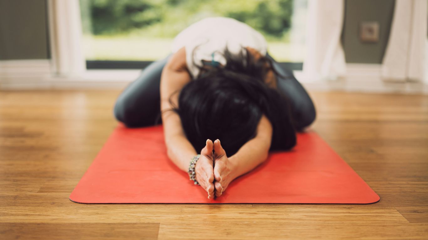 woman in white shirt lying on red mat on brown wooden table