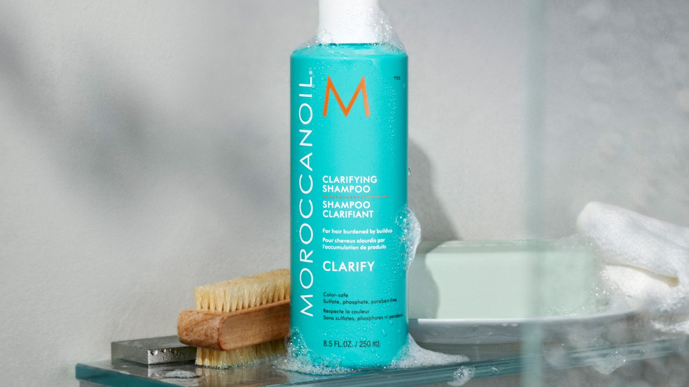 Bottle of clarifying shampoo with soap and brush in shower.