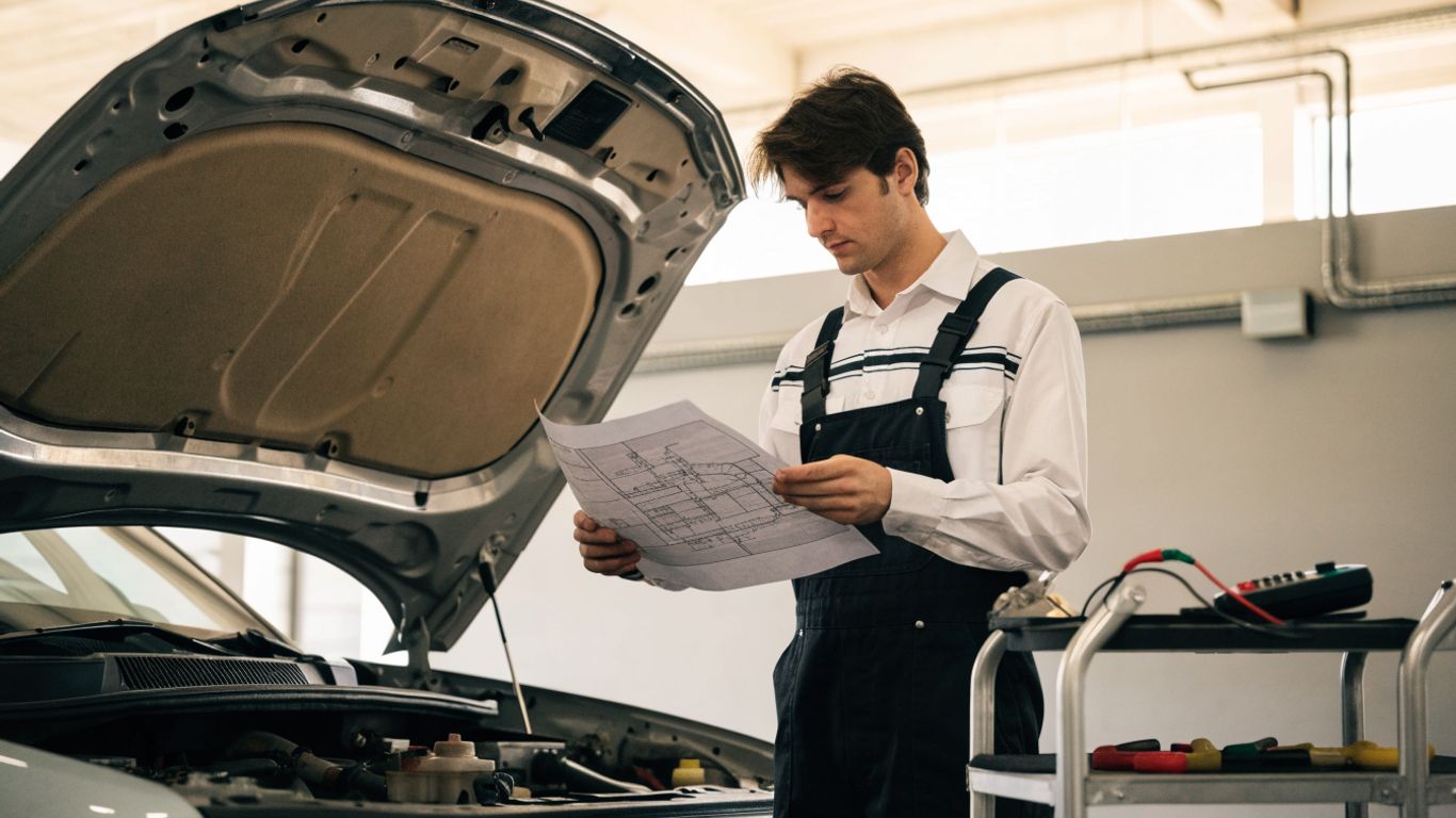 Technician reviewing vehicle wiring beside open hood