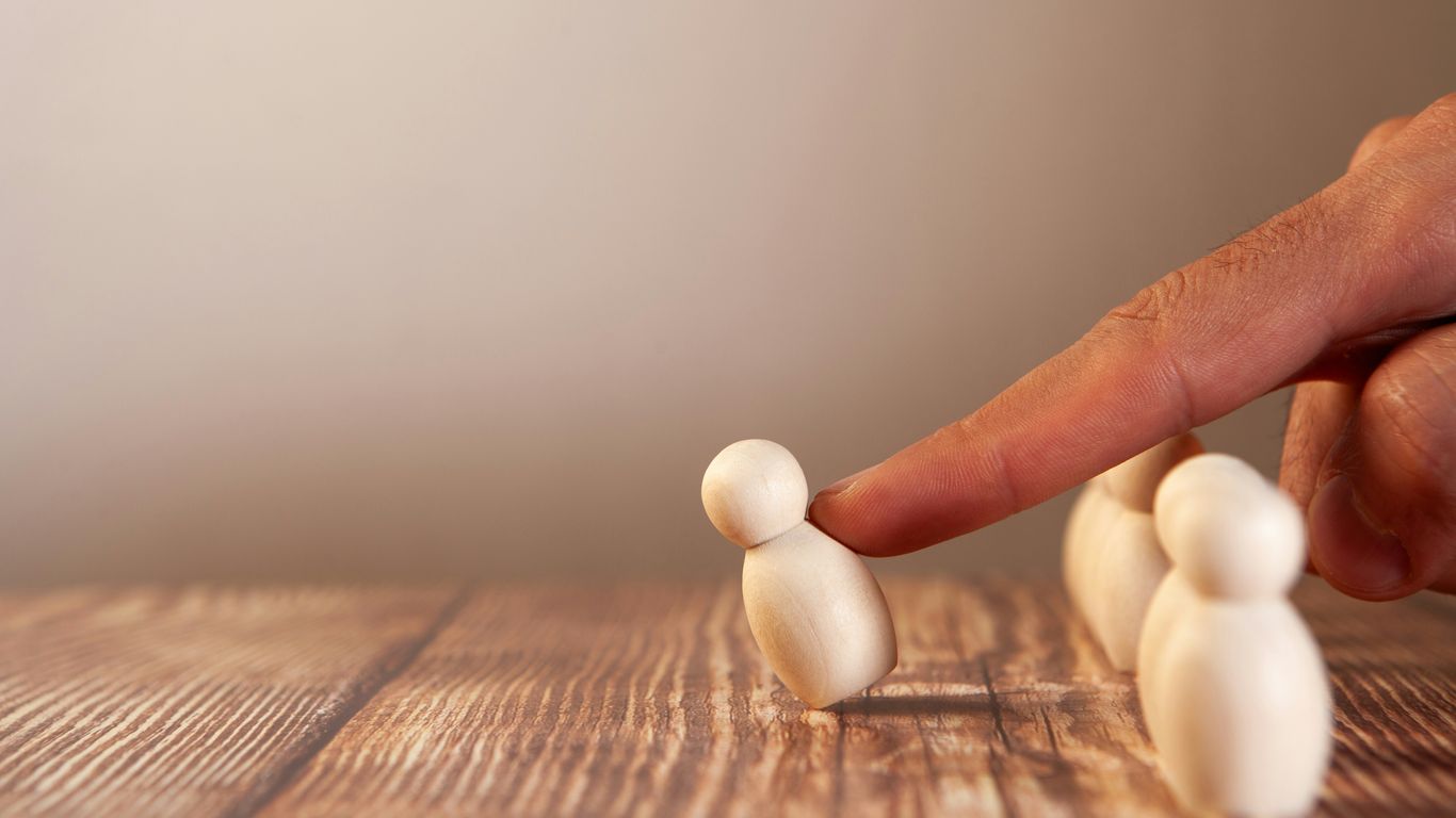 Finger pushing a small wooden figure over a group.