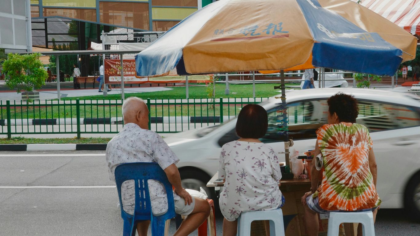 Three people sitting under an umbrella by the road