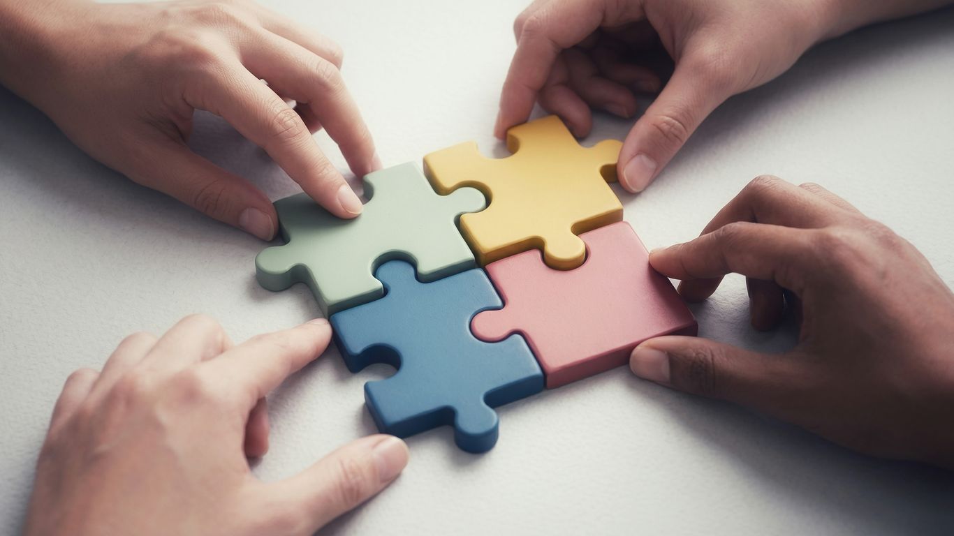 Hands connecting colorful puzzle pieces together.