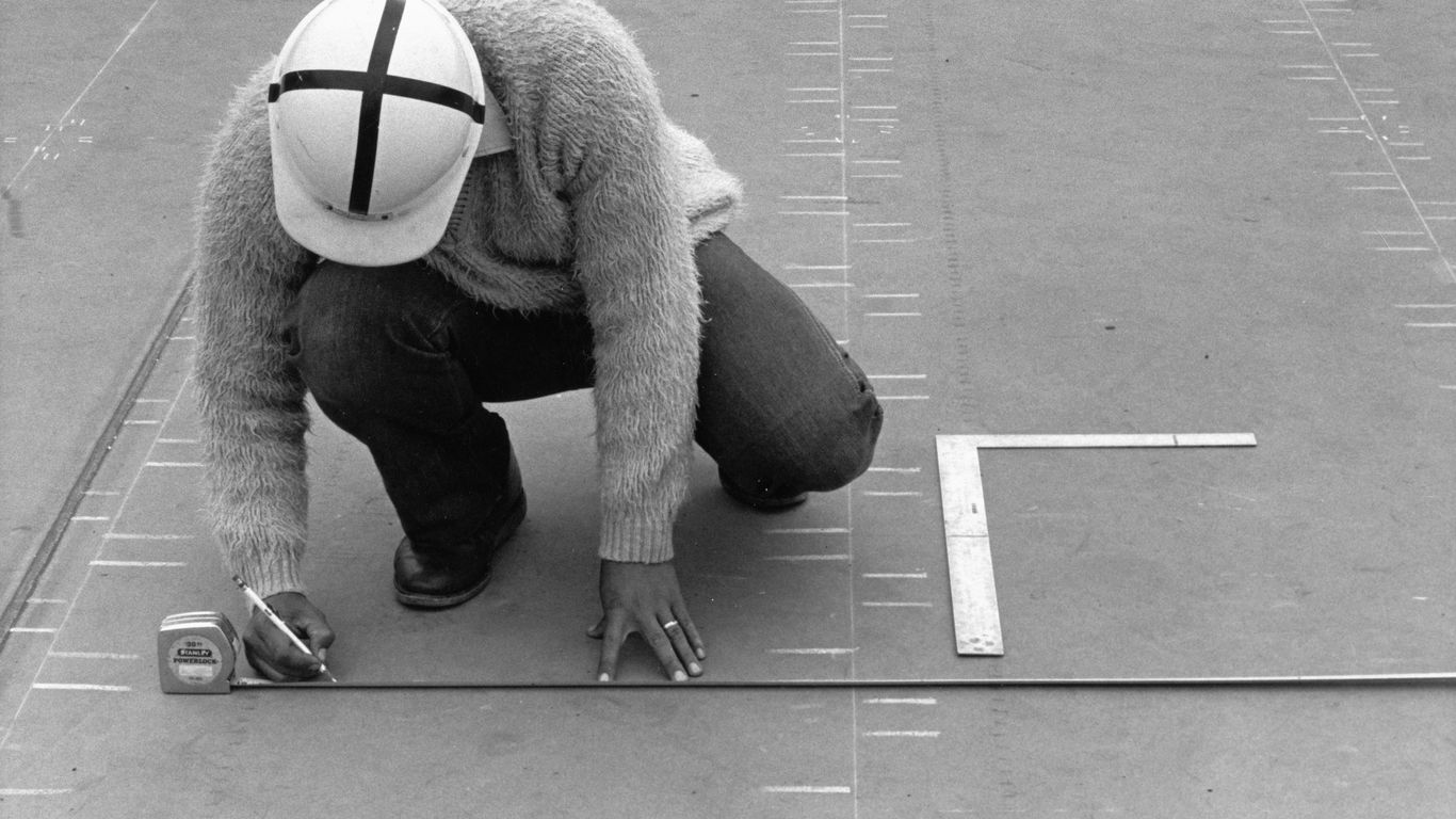 Worker measures a surface with a tape measure and pencil.