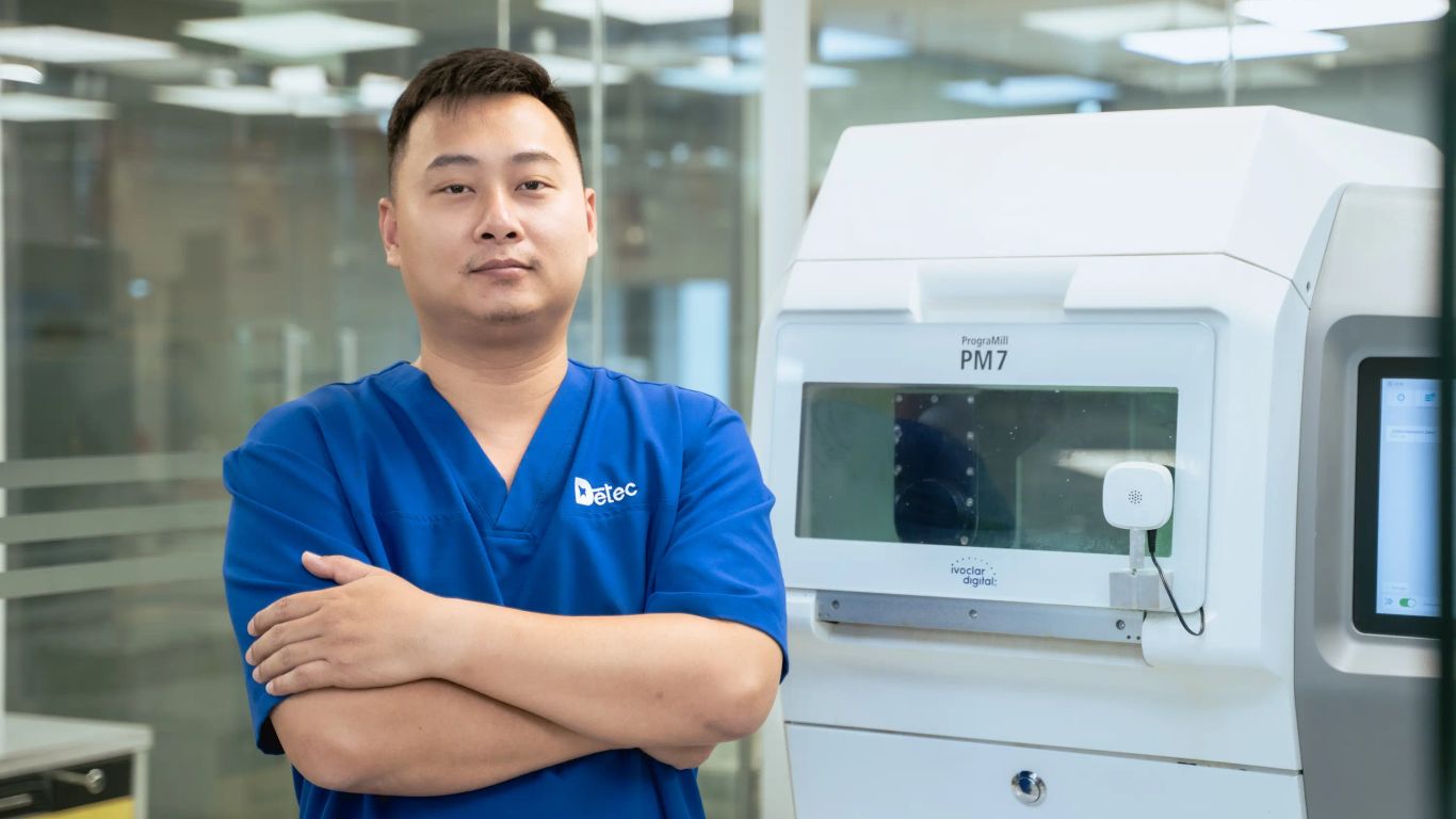 A person stands next to a white dental milling machine in a lab.