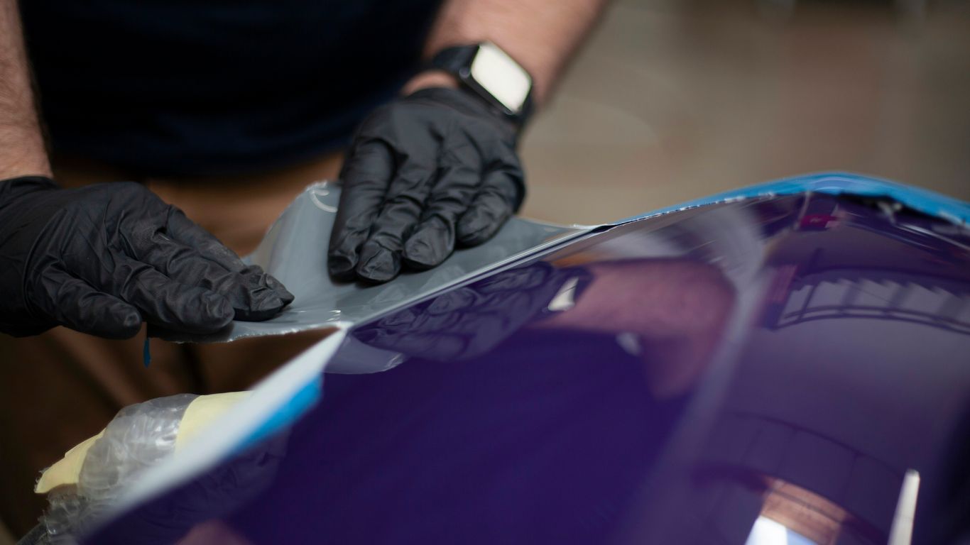 a man in black gloves waxing a blue car