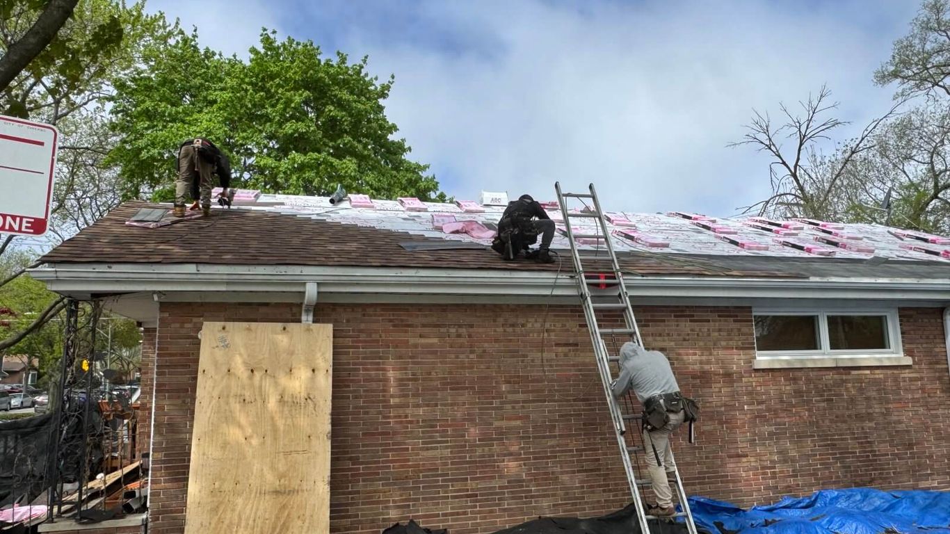 Workers on a ladder installing a new roof on a brick house.