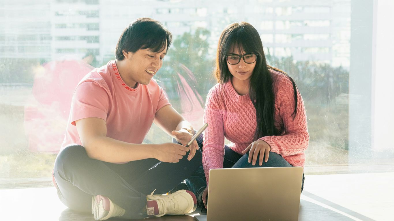A man and a woman sitting on the floor with a laptop