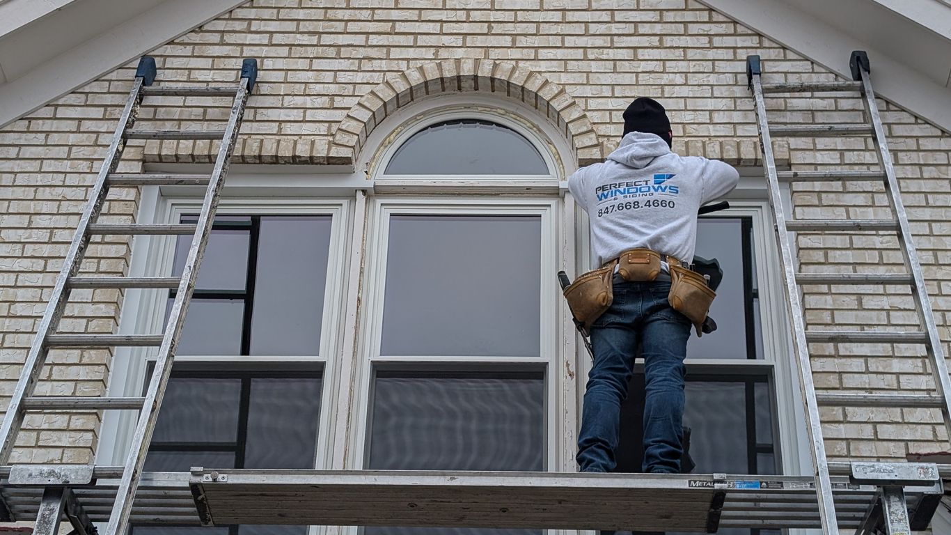 Worker on scaffolding installing windows on a brick house.