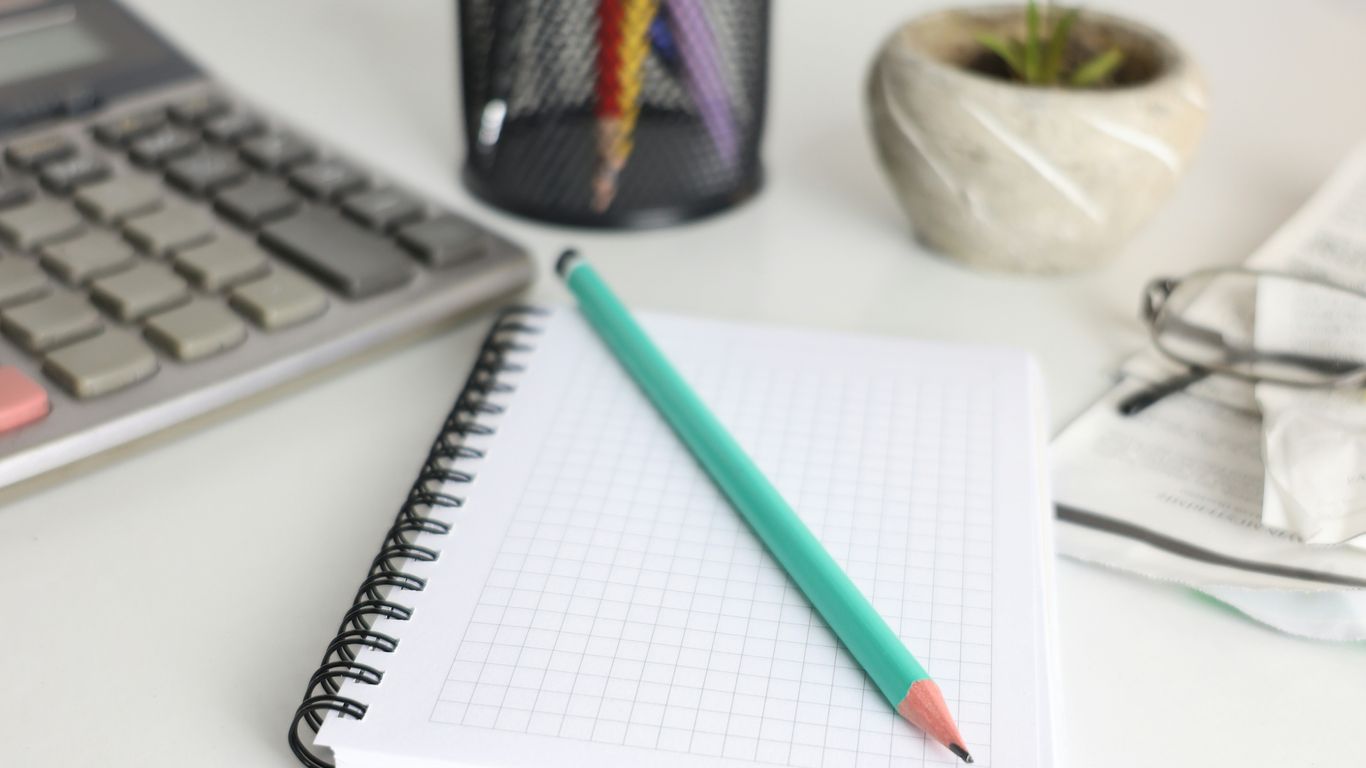 Desk with calculator, notebook, pencil, and plant.