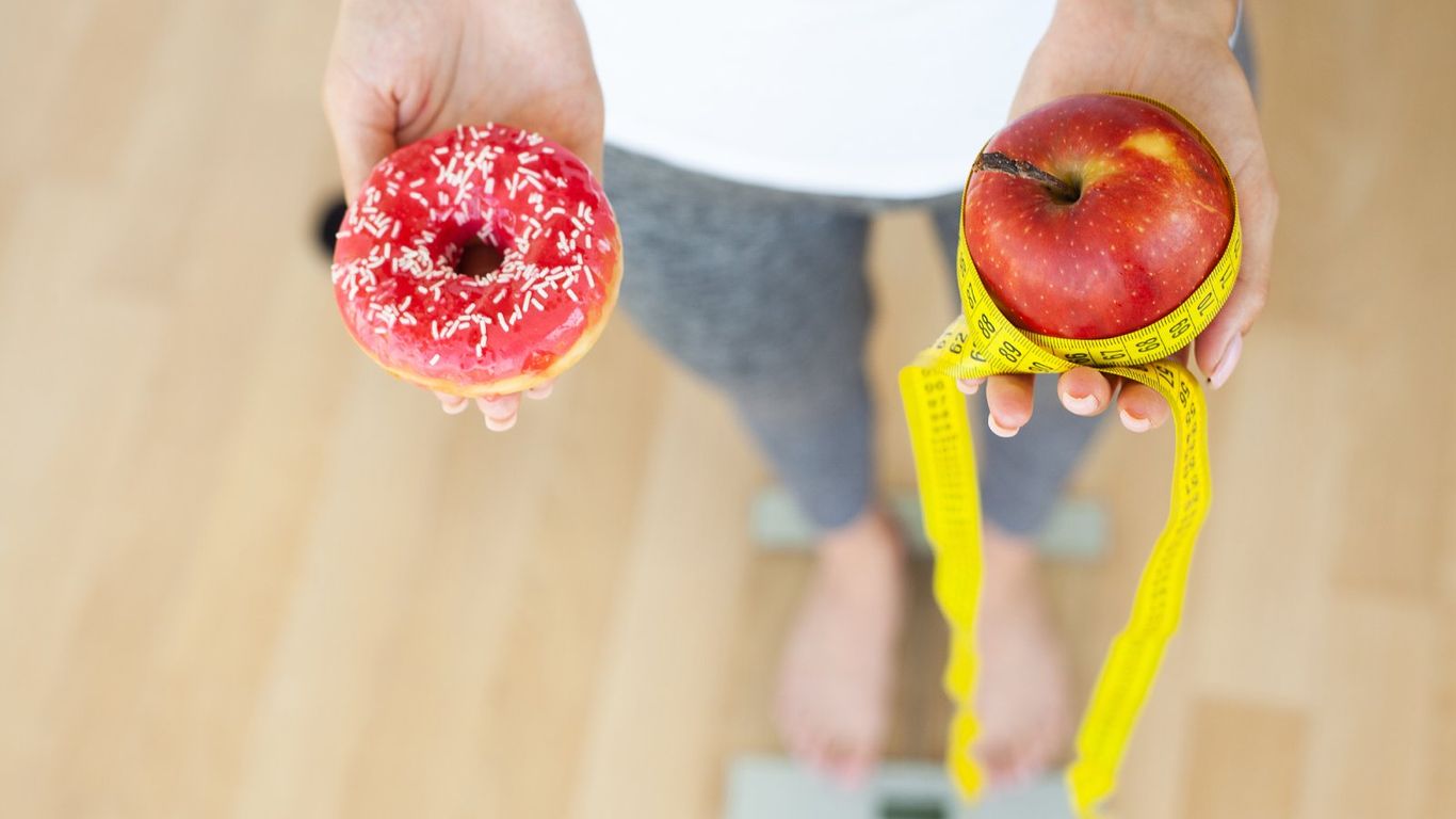 Person holding a donut and an apple with a measuring tape.
