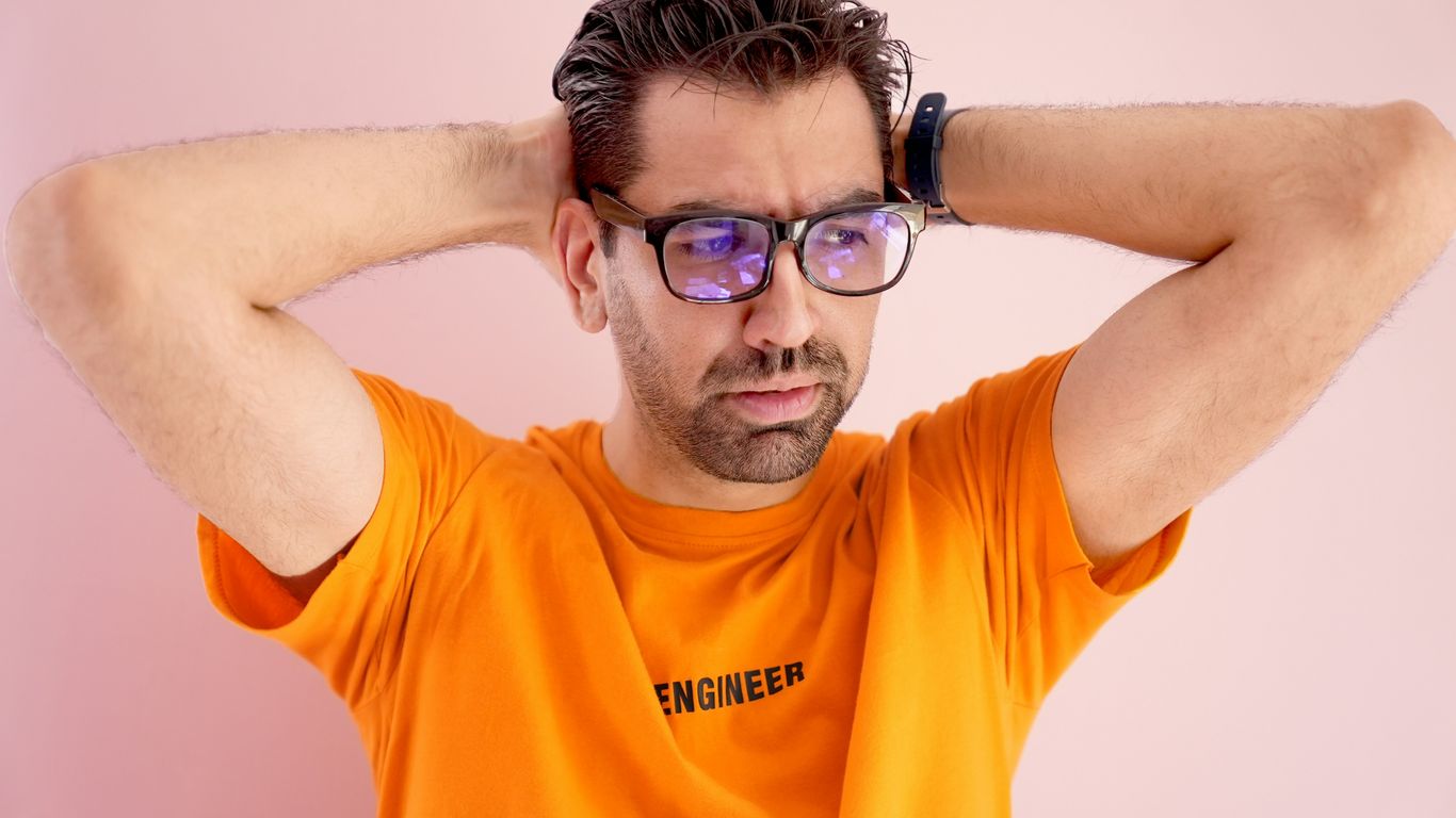 a man in an orange shirt is holding his head with his hands