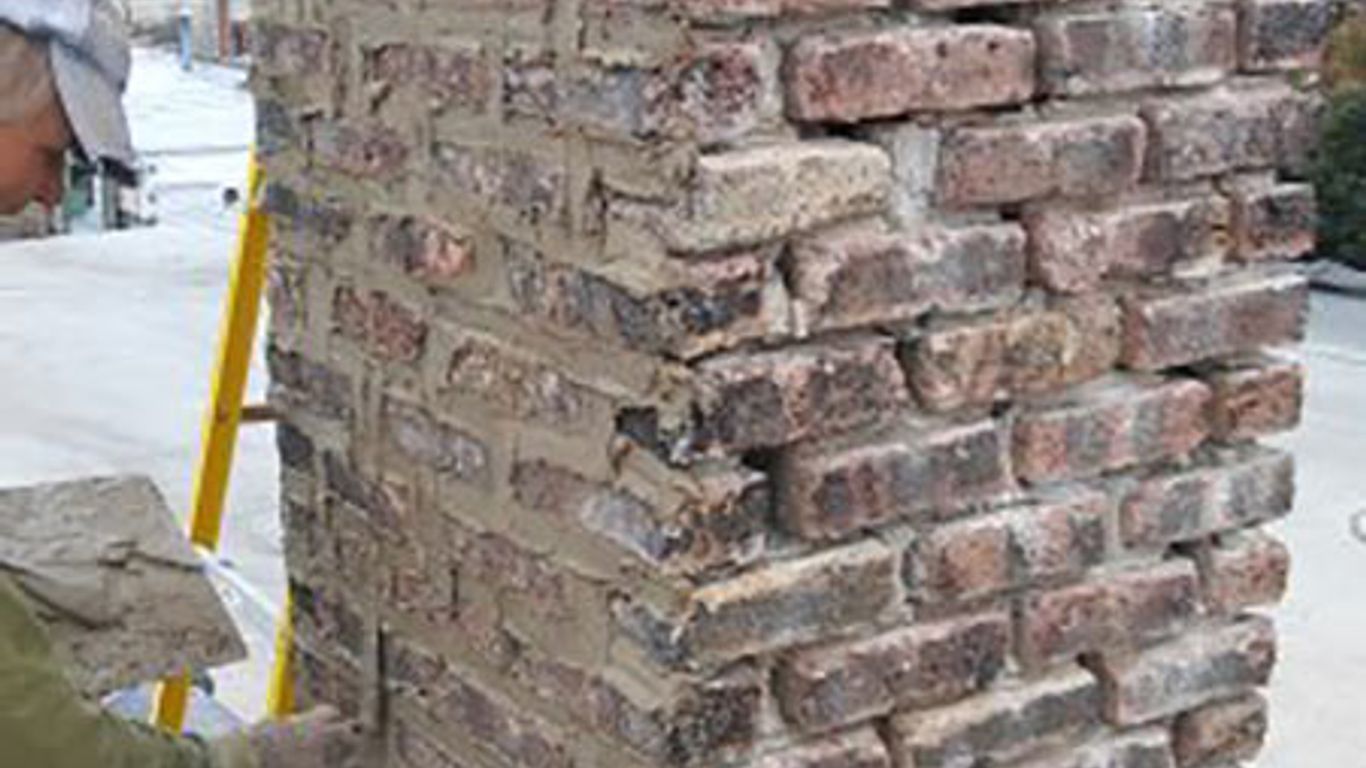 A person is repairing a brick chimney with mortar and bricks.